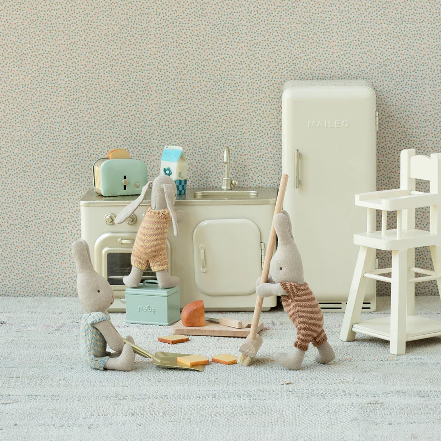 Children's play kitchen set with toy elephants and furniture against a neutral wall.