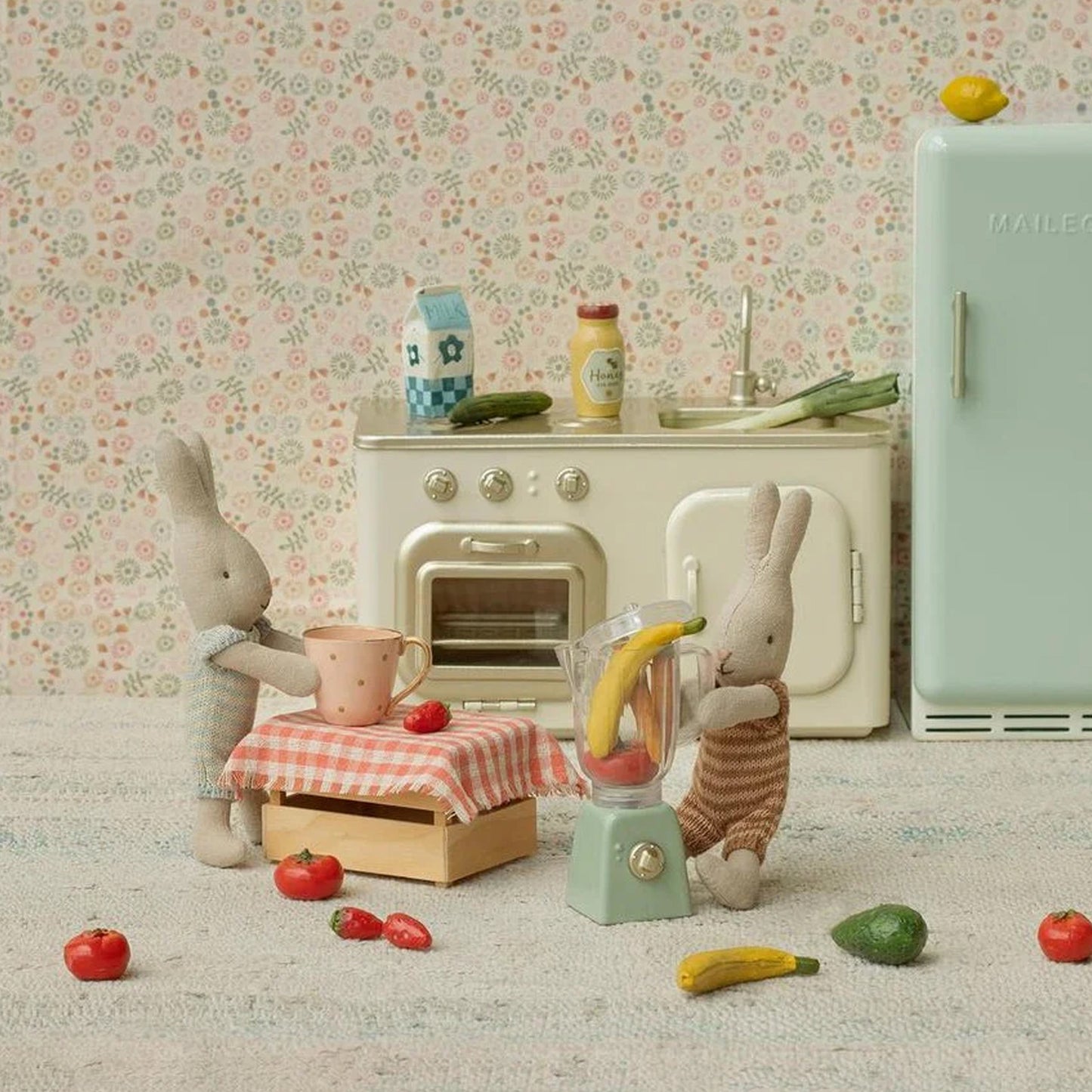 Miniature kitchen scene with toy rabbits and kitchen appliances against a floral wallpaper background.