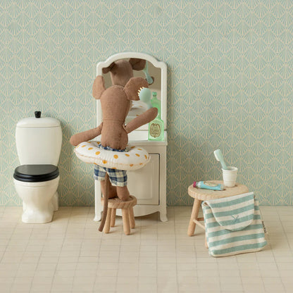 Stuffed teddy bear in a bathtub with bathroom items and wallpaper.