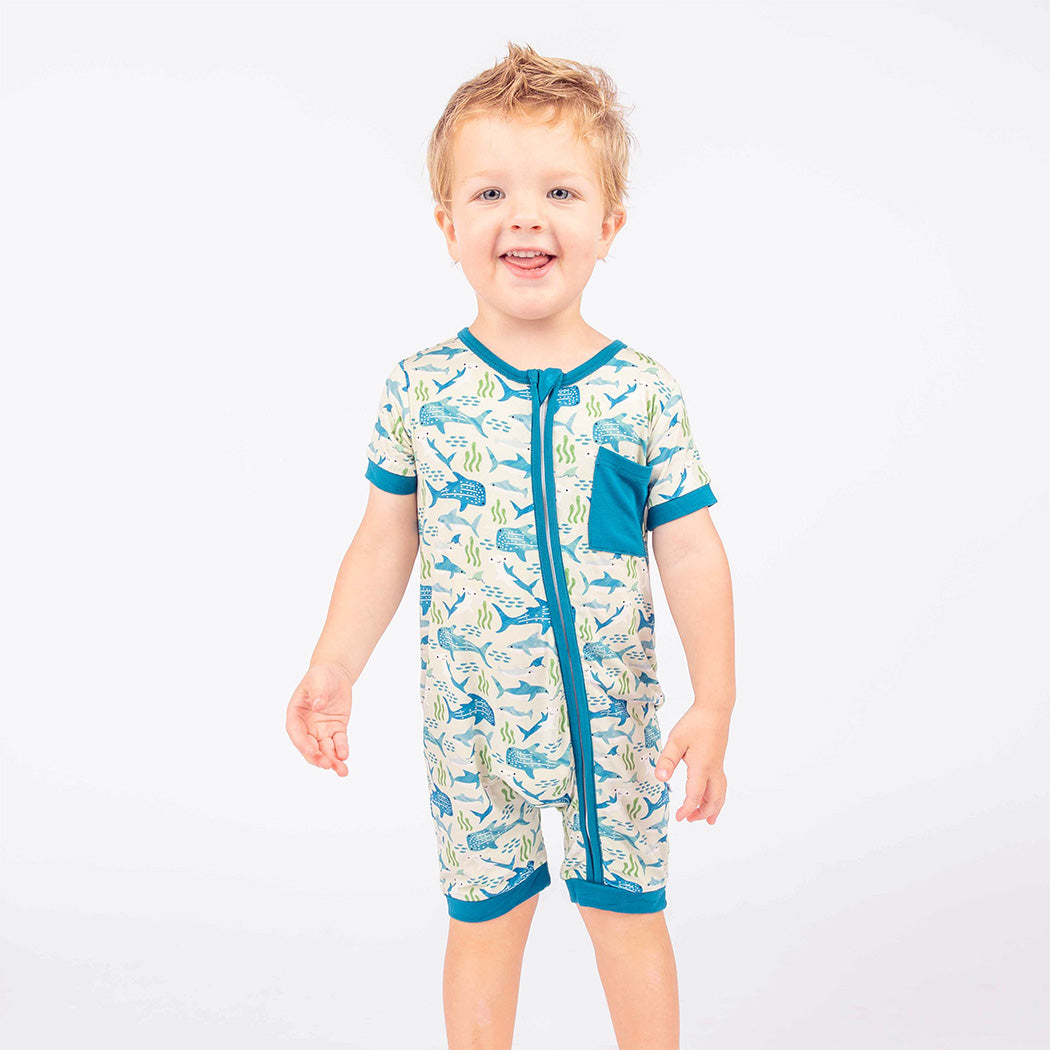 Little boy standing while wearing our Shark Friends Shortie Romper.