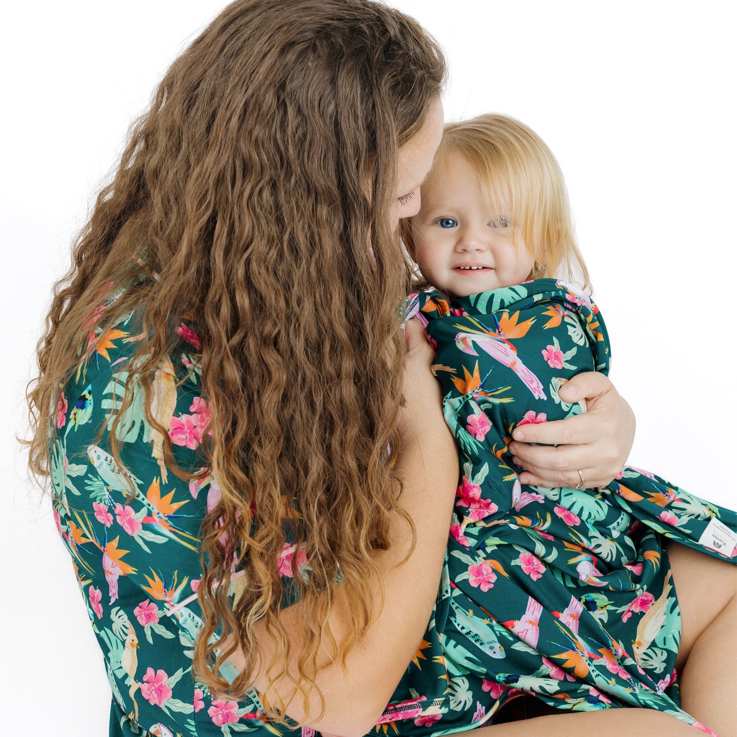 A mother and her children sitting together in matching Isla Botánica tropical birds print pajamas for a coordinated family look.