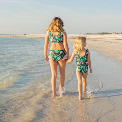 A mother and daughter walking on the beach in matching Isla Botánica tropical print swimwear.
