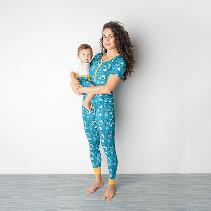 mom stand up against a wall wearing her "ocean friends" women's top and jogger bottoms. she holds her baby on her hip. the "ocean friends" print is a combination of dolphins, stingrays, fish, starfish, coral, bubbles, and sharks, all spread out on a deep sea blue background.