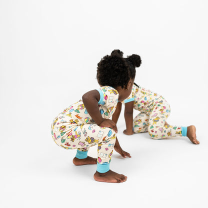 Matching siblings wearing our Arthur's Family Vacation Bamboo Short Sleeve Kids Pajama Pants Set featuring vibrant light blue trim and a playful print of Arthur™ in swimwear surrounded by fun beach props — perfect for family getaways.