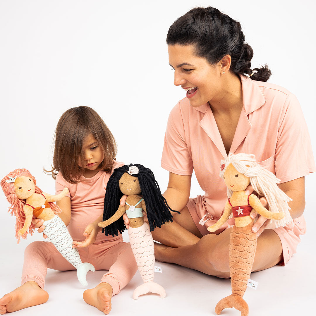 mom and girl play with Adriana the stuffed plush mermaid. she is a blonde mermaid with a red top and orange tail. 