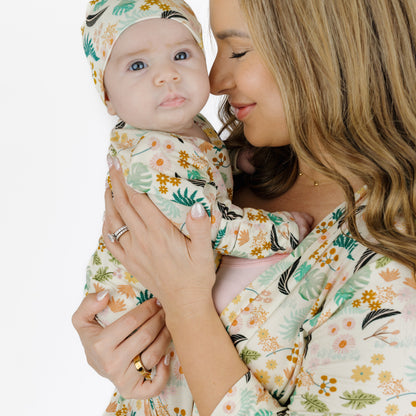 A mother holding her newborn baby who is dressed in the matching Tropical Blooms bamboo gown and hat set.