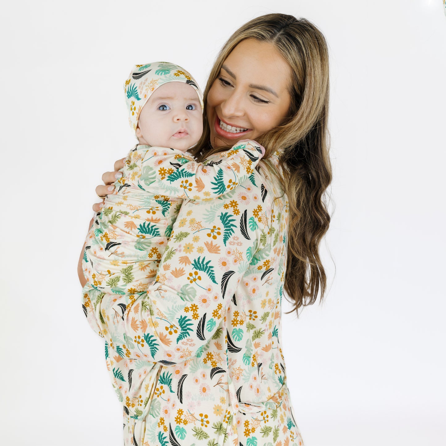 A mother holding her newborn baby who is dressed in the matching Tropical Blooms bamboo gown and hat set.