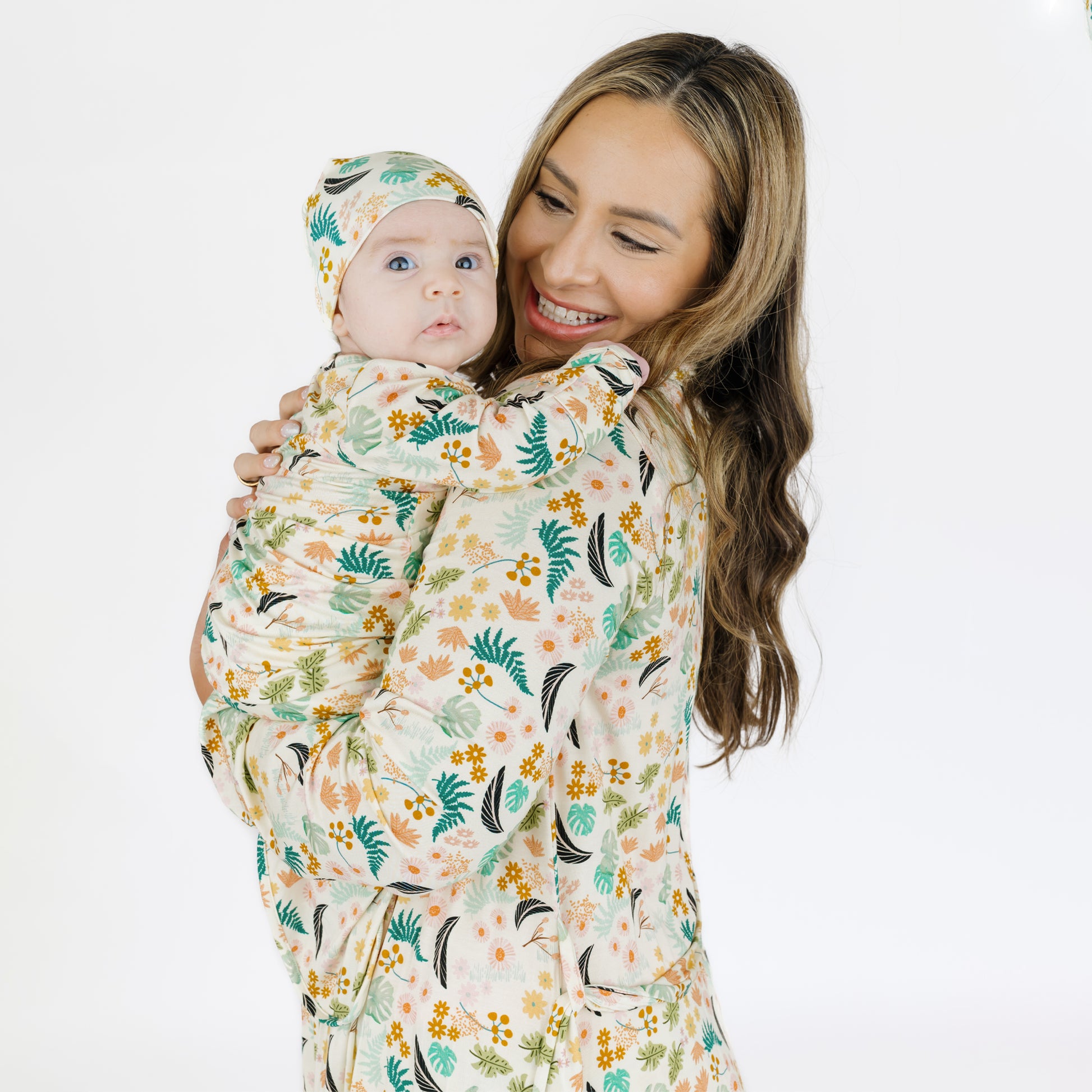 A mother holding her newborn baby who is dressed in the matching Tropical Blooms bamboo gown and hat set.
