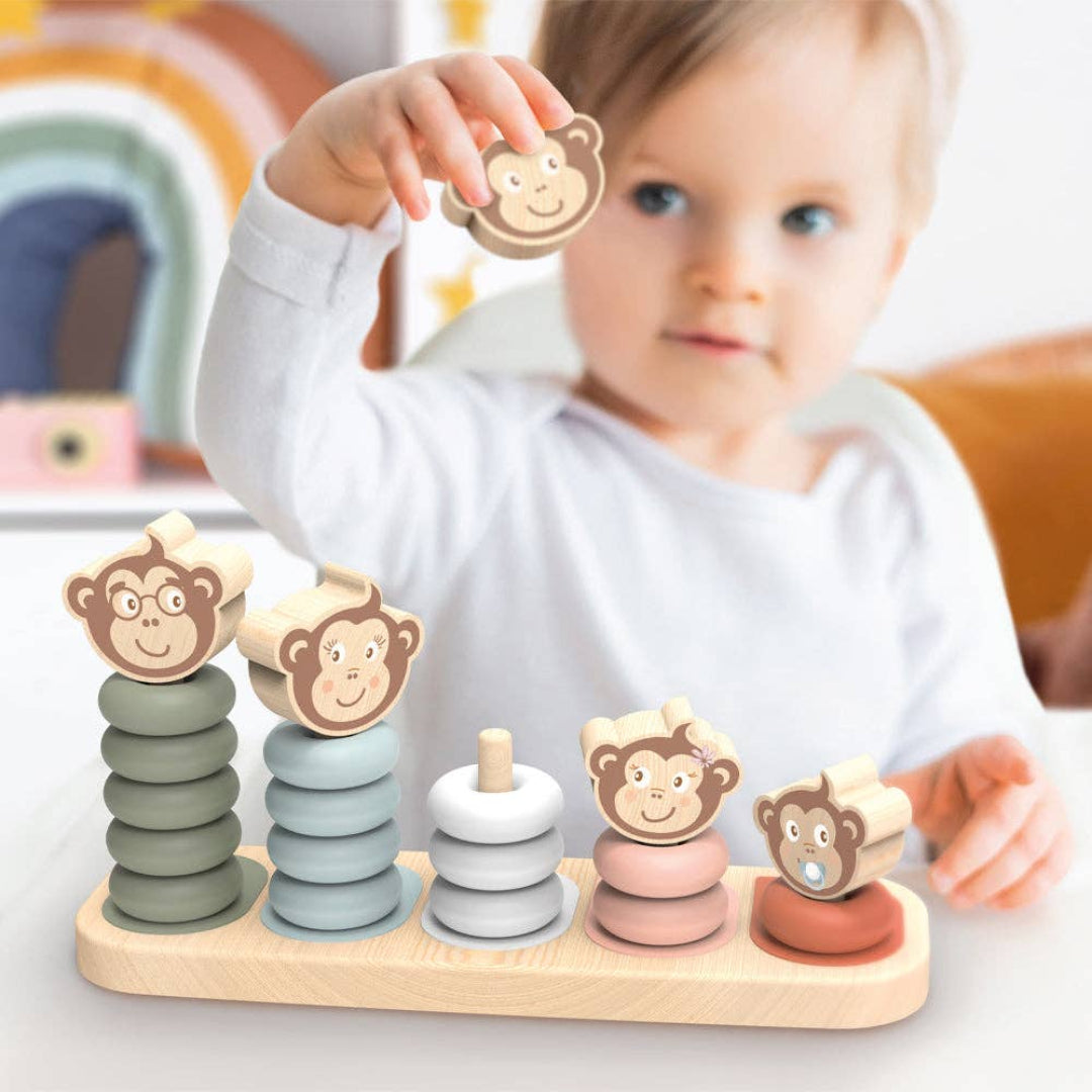 wooden stacking toy with 5 different height posts to stack round blocks on, ranging from short to tall. The blocks are red, pink, light blue, dark blue and green and they all have a monkey head smiling on top