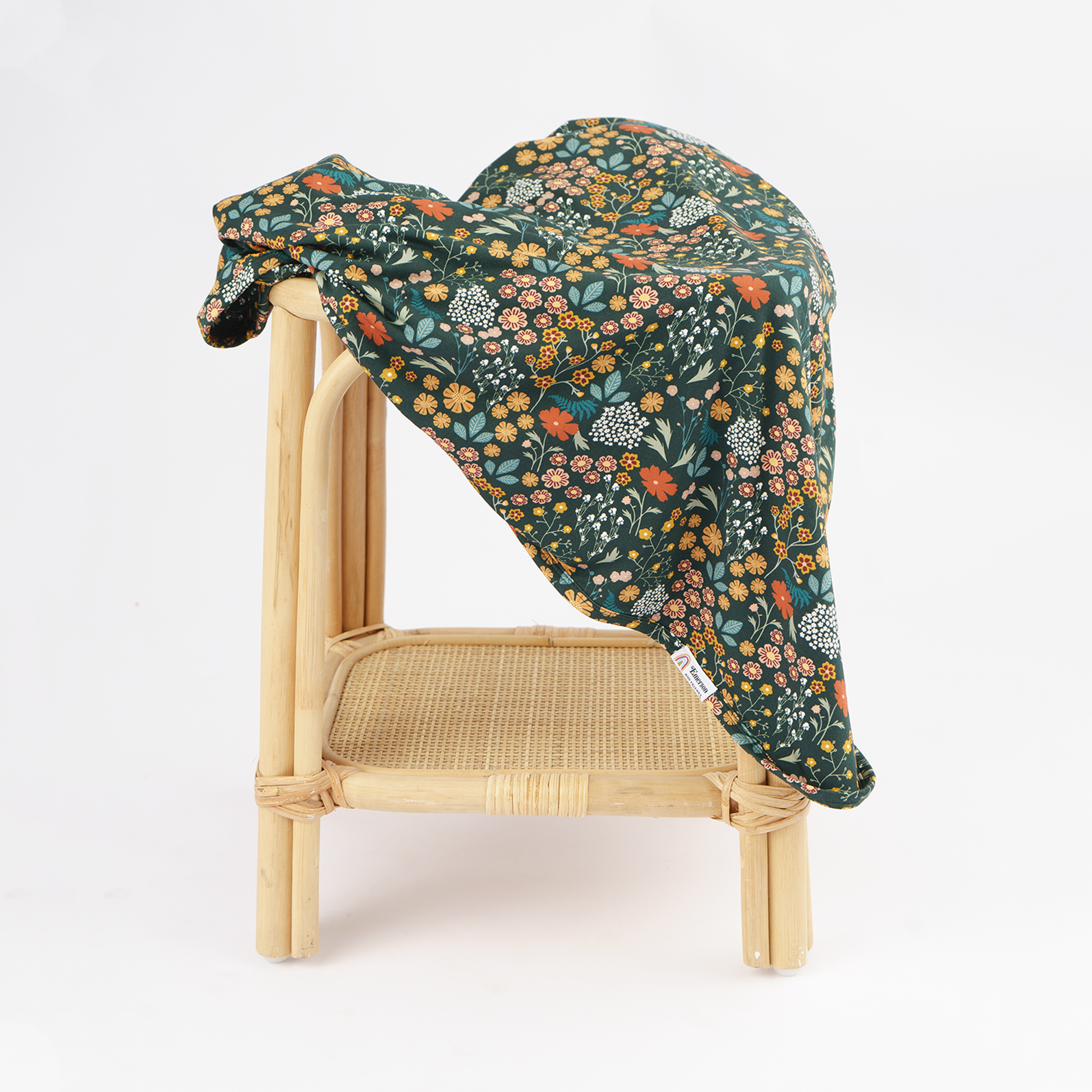 A dark green floral blanket draped over a light natural wood rattan chair against a clean white background.