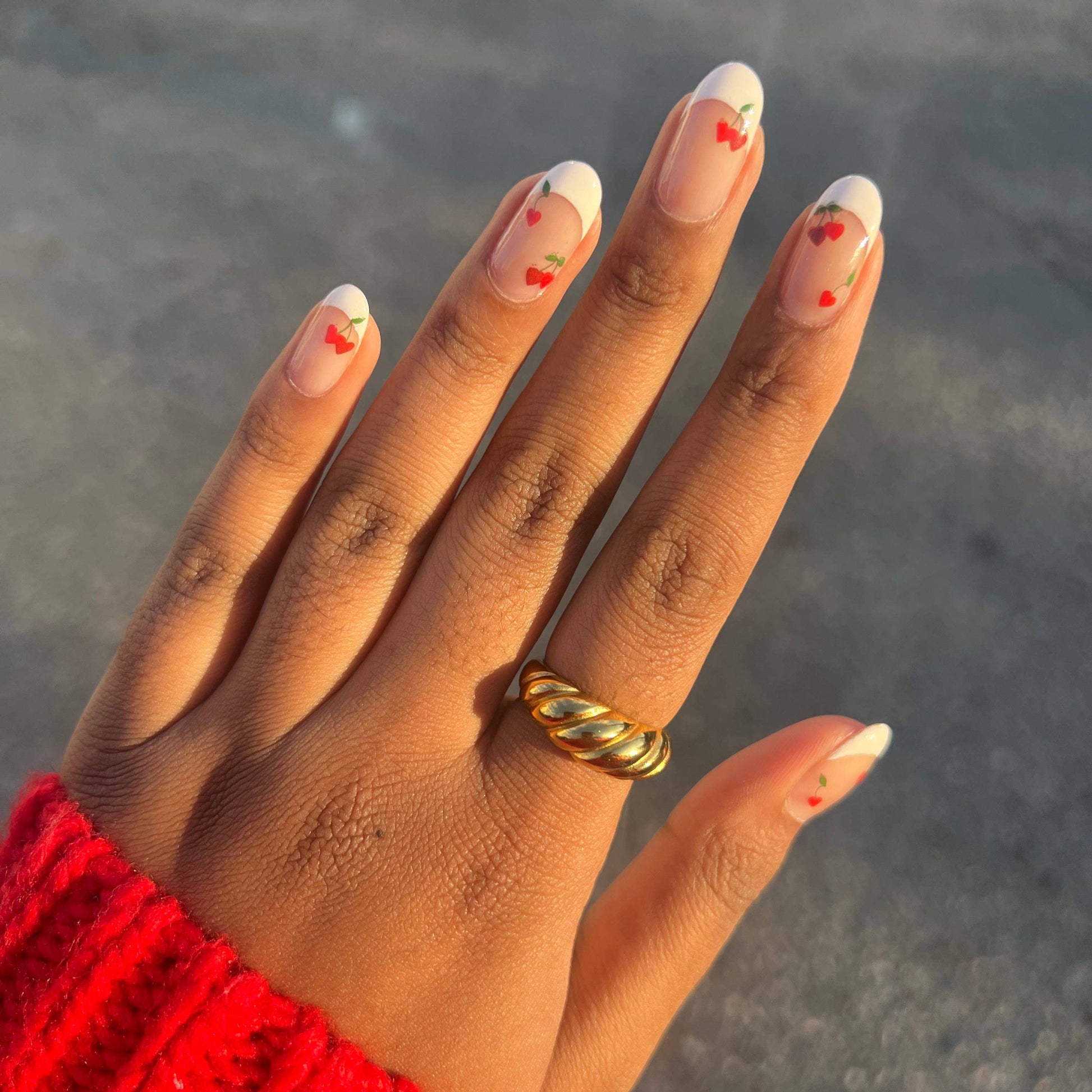 Hand with red nail polish and a gold ring, wearing a red sleeve against a blurred background