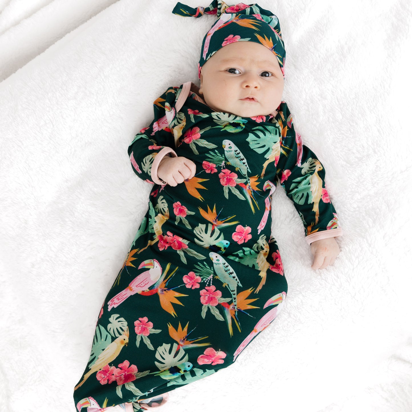 A newborn baby laying down in the Isla Botánica bamboo tie gown and hat set, perfect for hospital or first photos.