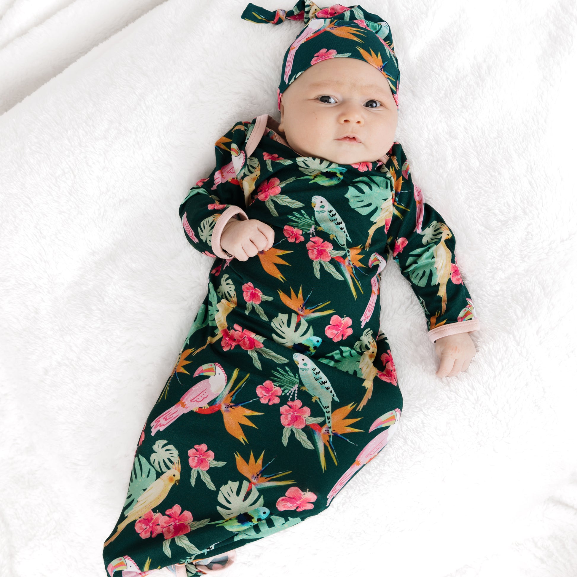 A newborn baby laying down in the Isla Botánica bamboo tie gown and hat set, perfect for hospital or first photos.