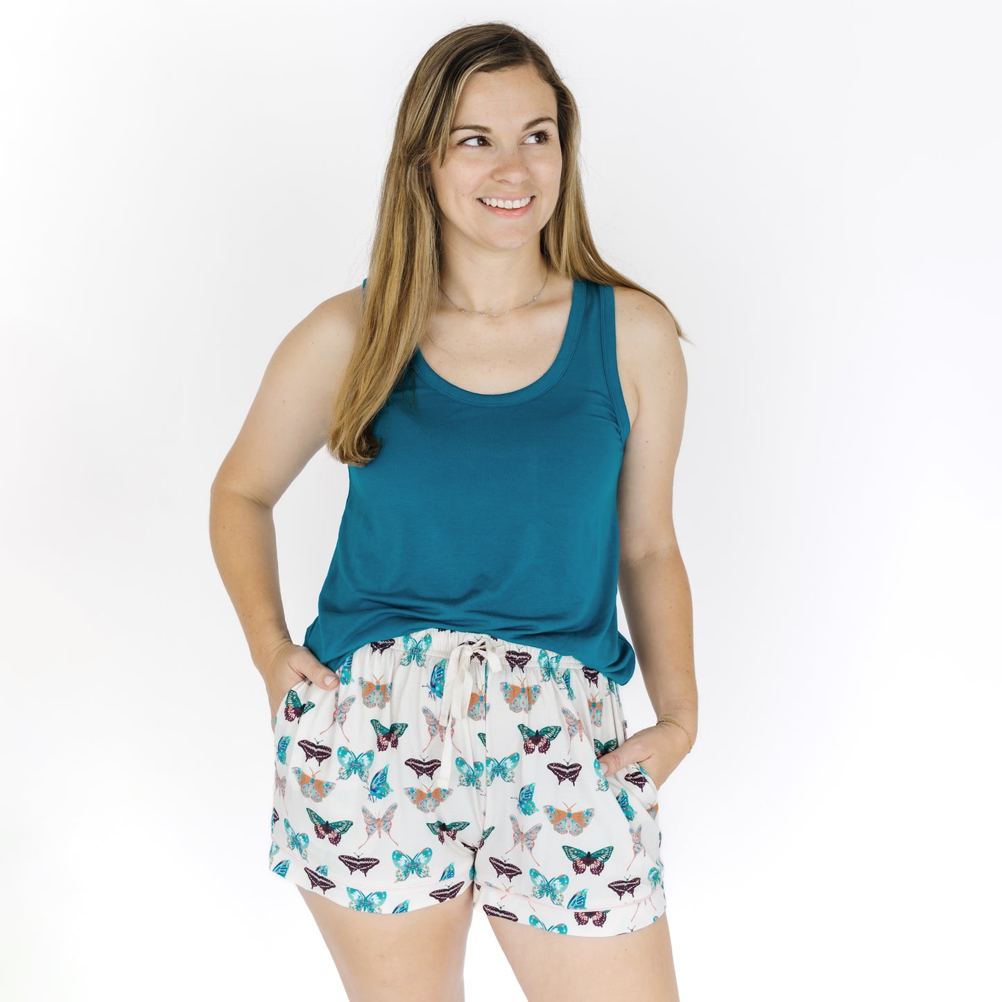Woman wearing a teal tank top and butterfly patterned shorts on a white background