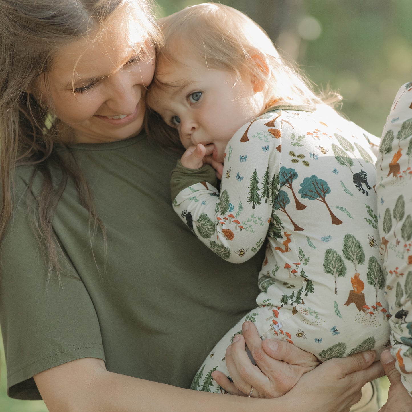 Woman holding a child in a patterned outfit outdoors