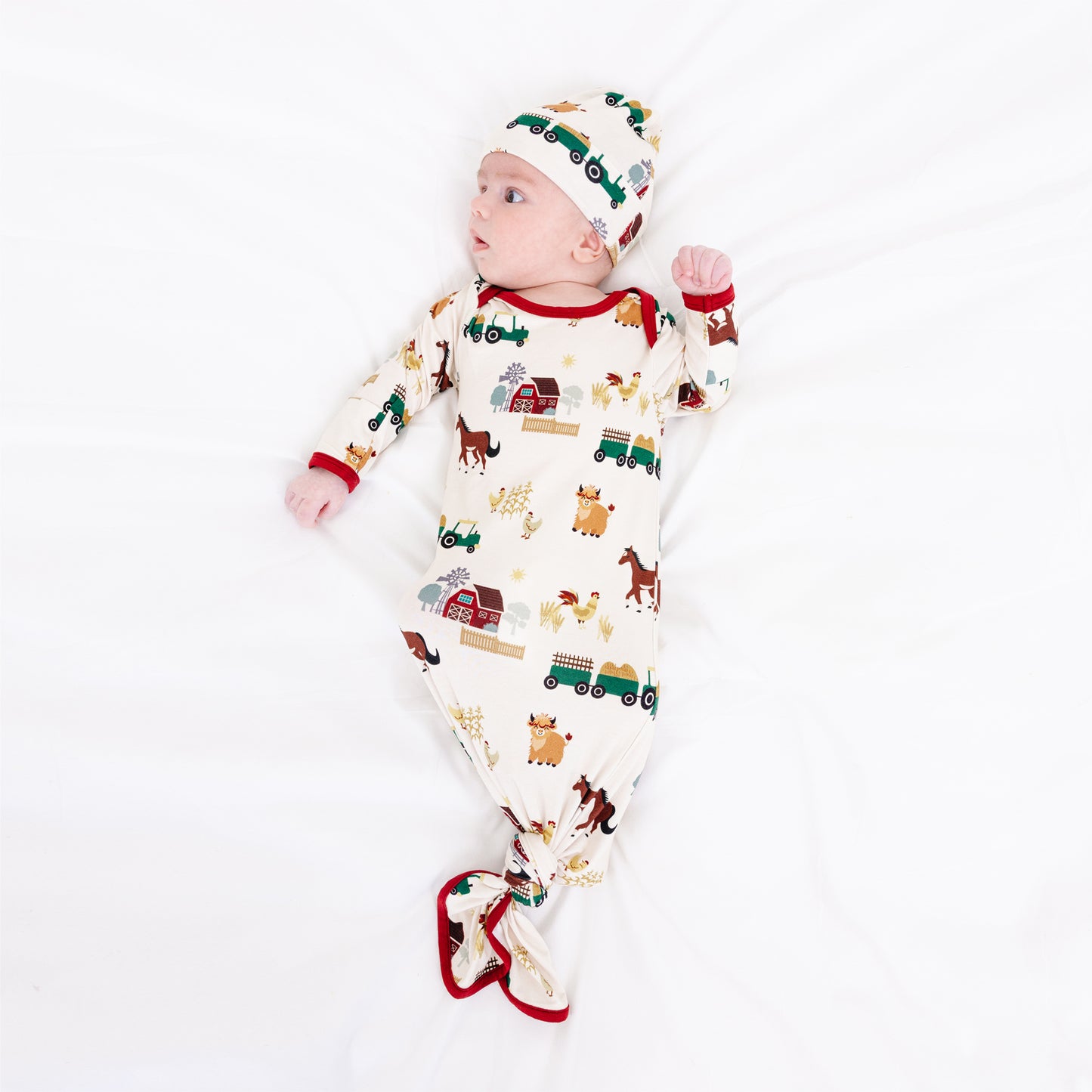 Newborn wearing On the Farm bamboo baby gown and hat set with farm print of horses and tractors, soft and breathable for sensitive skin.