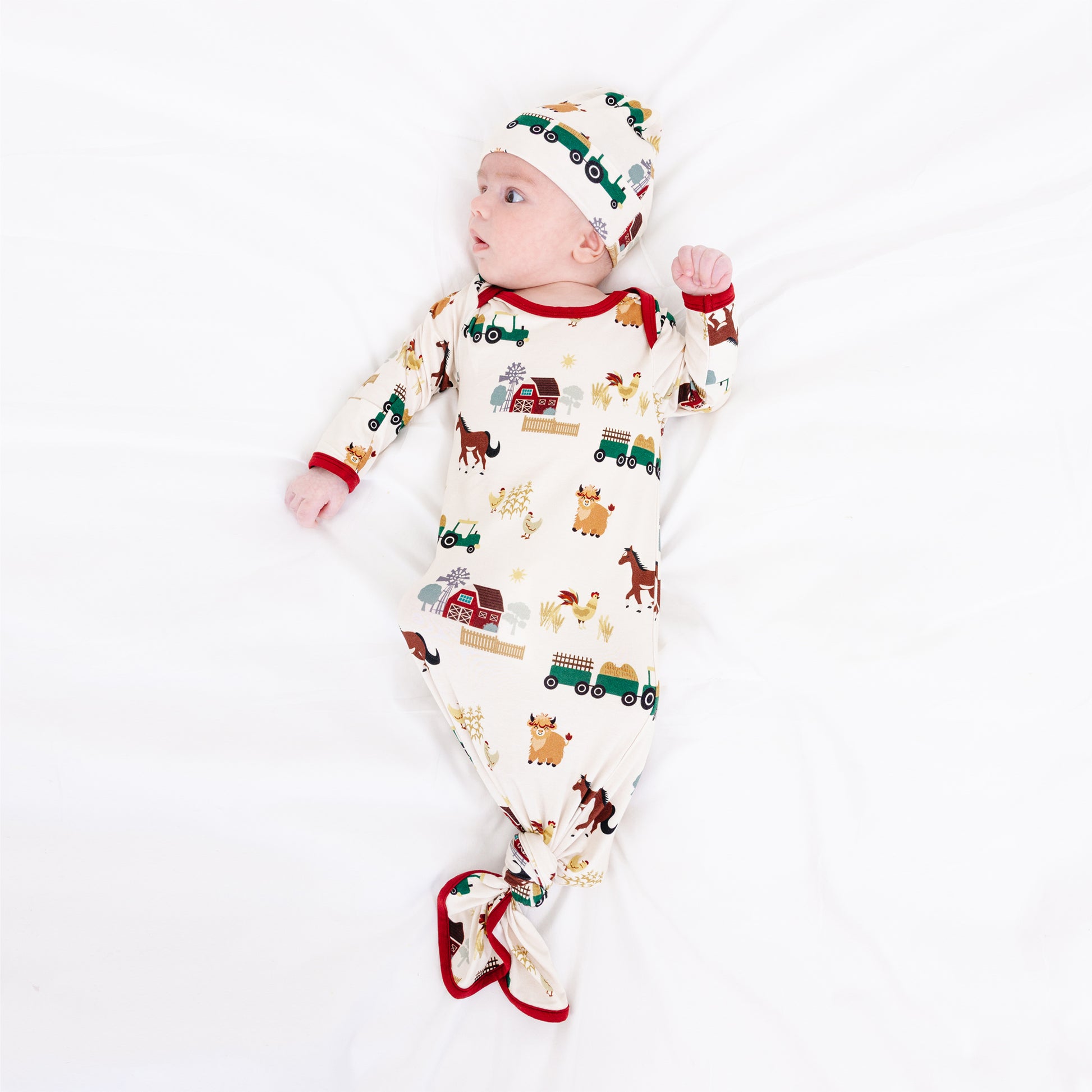 Newborn wearing On the Farm bamboo baby gown and hat set with farm print of horses and tractors, soft and breathable for sensitive skin.