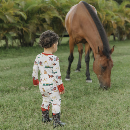 On the Farm bamboo convertible pajamas with horse, cow, and tractor print, shown outdoors near a horse.