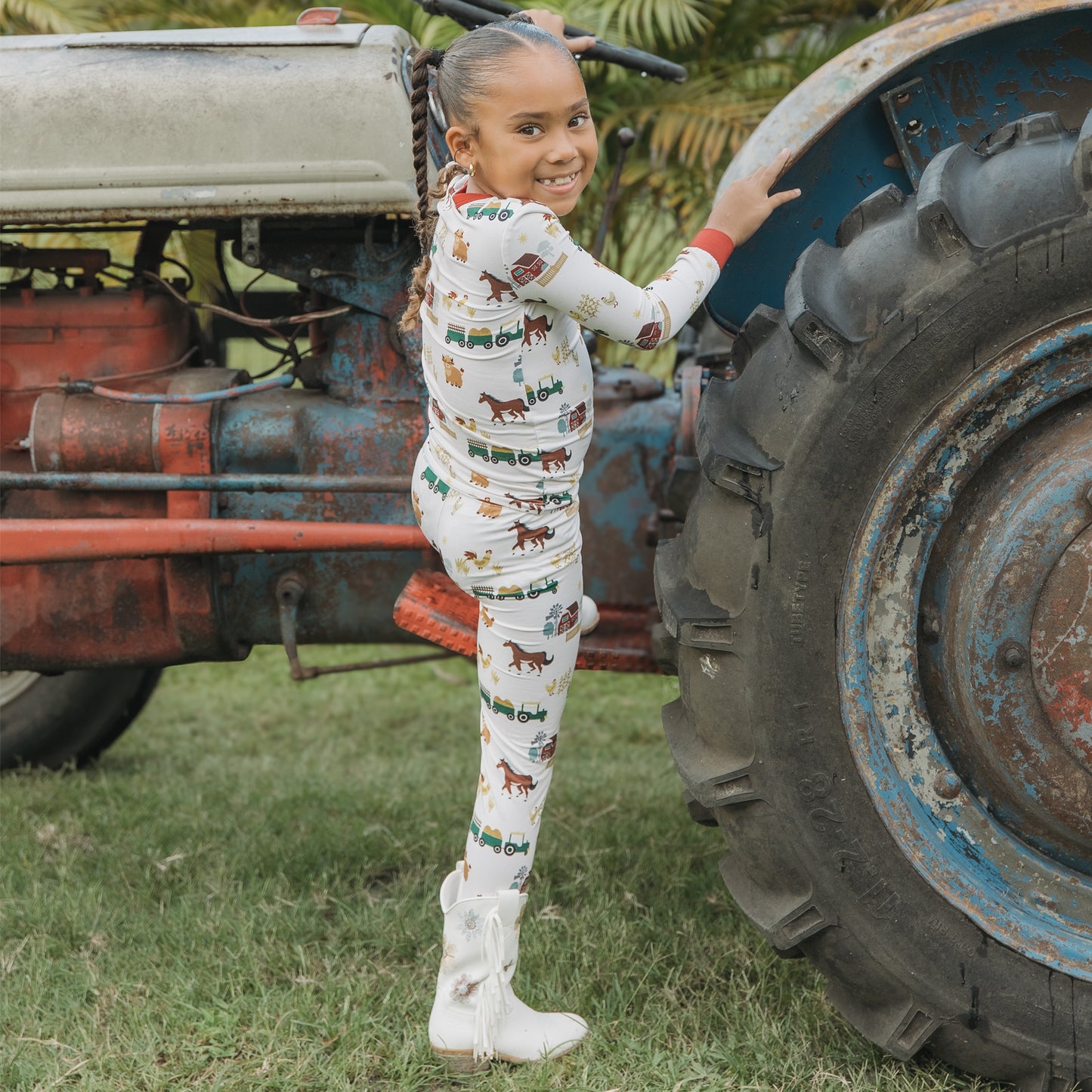 On the Farm bamboo kids pajama pants set with tractors, horses, and cows, shown outdoors by a tractor.