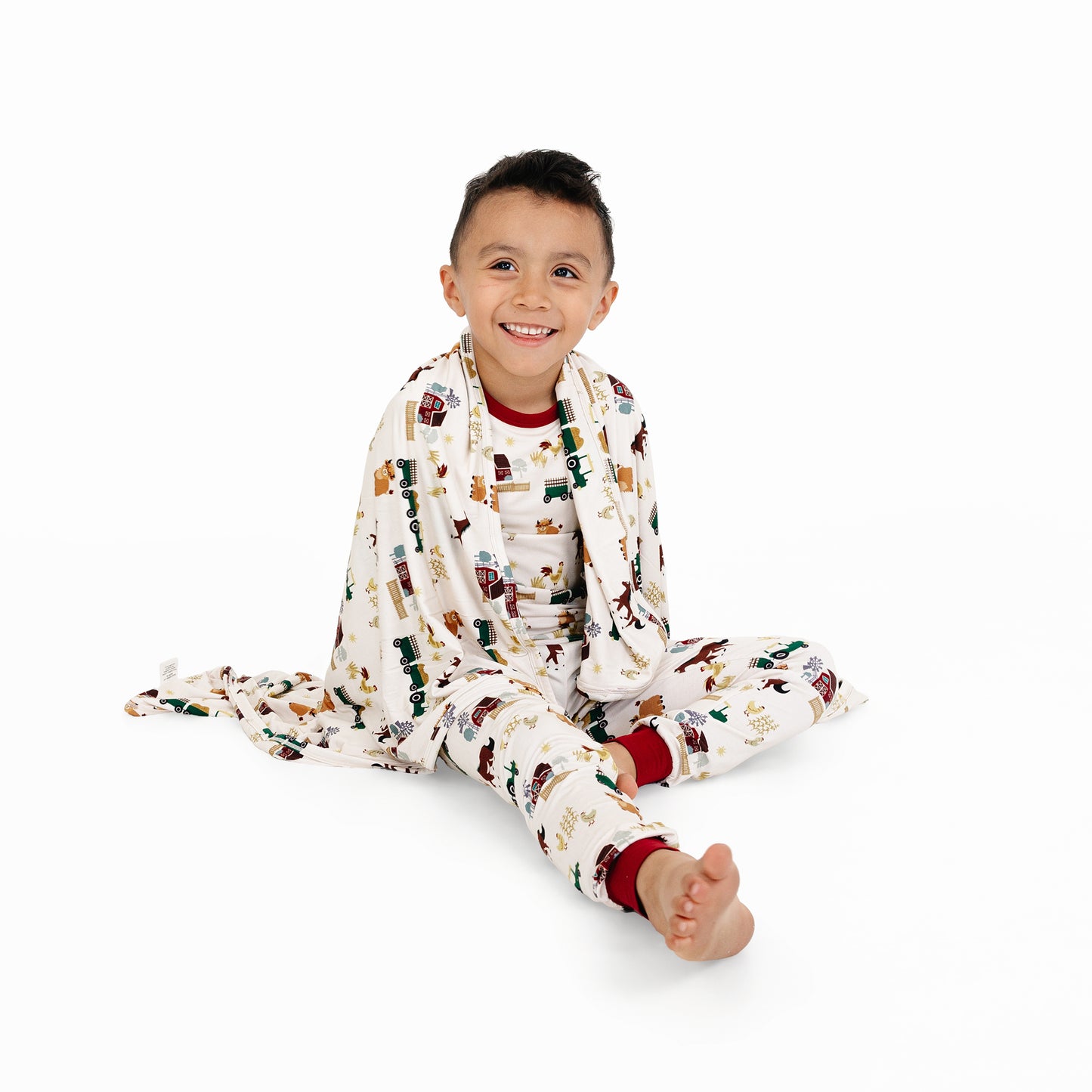 Child sitting wrapped in On the Farm luxury bamboo blanket with barnyard print of horses and tractors, soft and hypoallergenic bamboo fabric.
