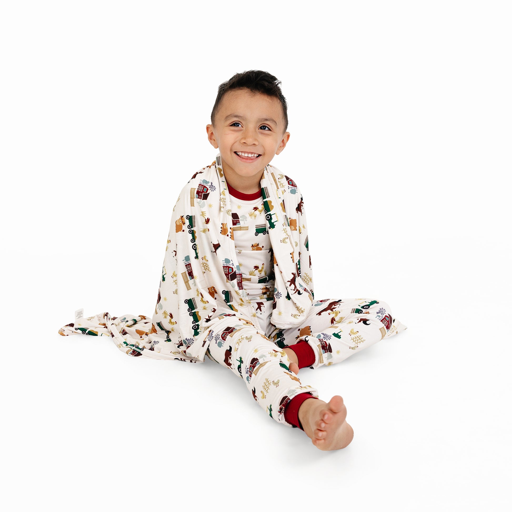 Child sitting wrapped in On the Farm luxury bamboo blanket with barnyard print of horses and tractors, soft and hypoallergenic bamboo fabric.