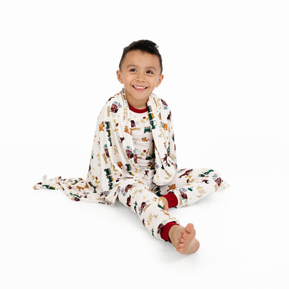 Child sitting wrapped in On the Farm luxury bamboo blanket with barnyard print of horses and tractors, soft and hypoallergenic bamboo fabric.