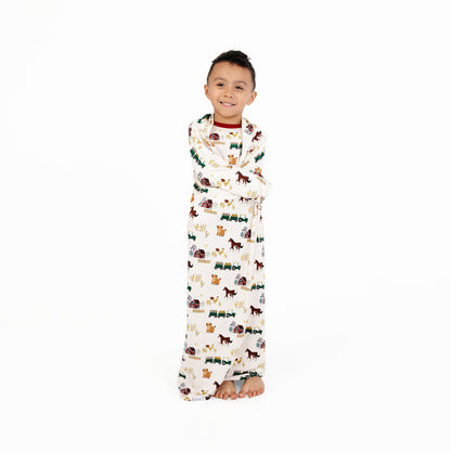 Child standing wrapped in On the Farm luxury bamboo blanket with farm animal print, breathable and hypoallergenic for sensitive skin.