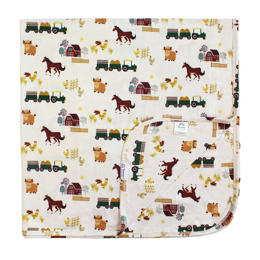 Flat lay of On the Farm luxury bamboo blanket with horse and tractor farm print, soft, breathable, and hypoallergenic for sensitive skin.