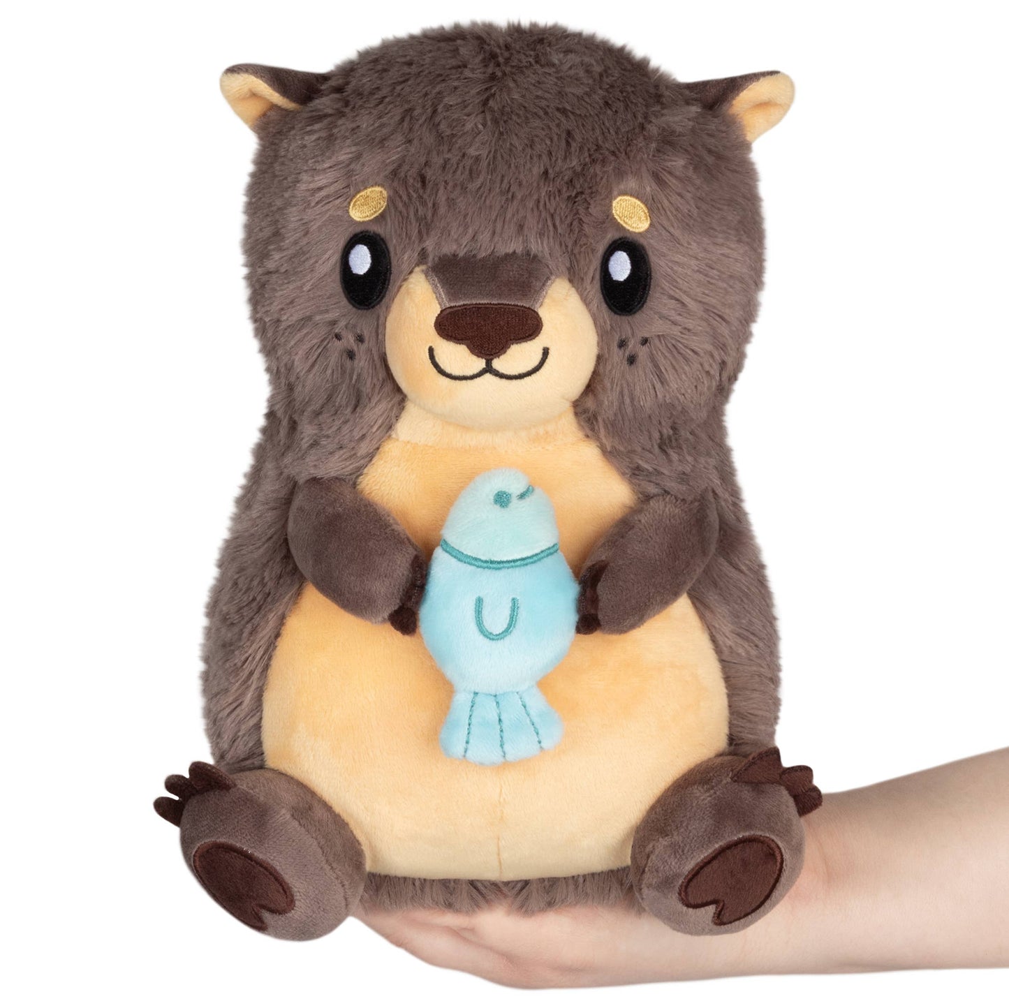 Plush toy otter holding a blue fish toy on a white background