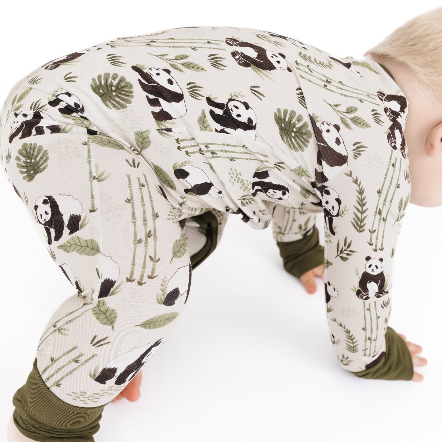 Baby in a onesie with panda and leaf pattern on a white background