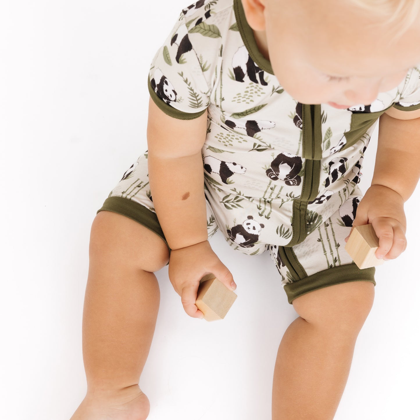 Baby in a panda-themed onesie holding a wooden block on a white background