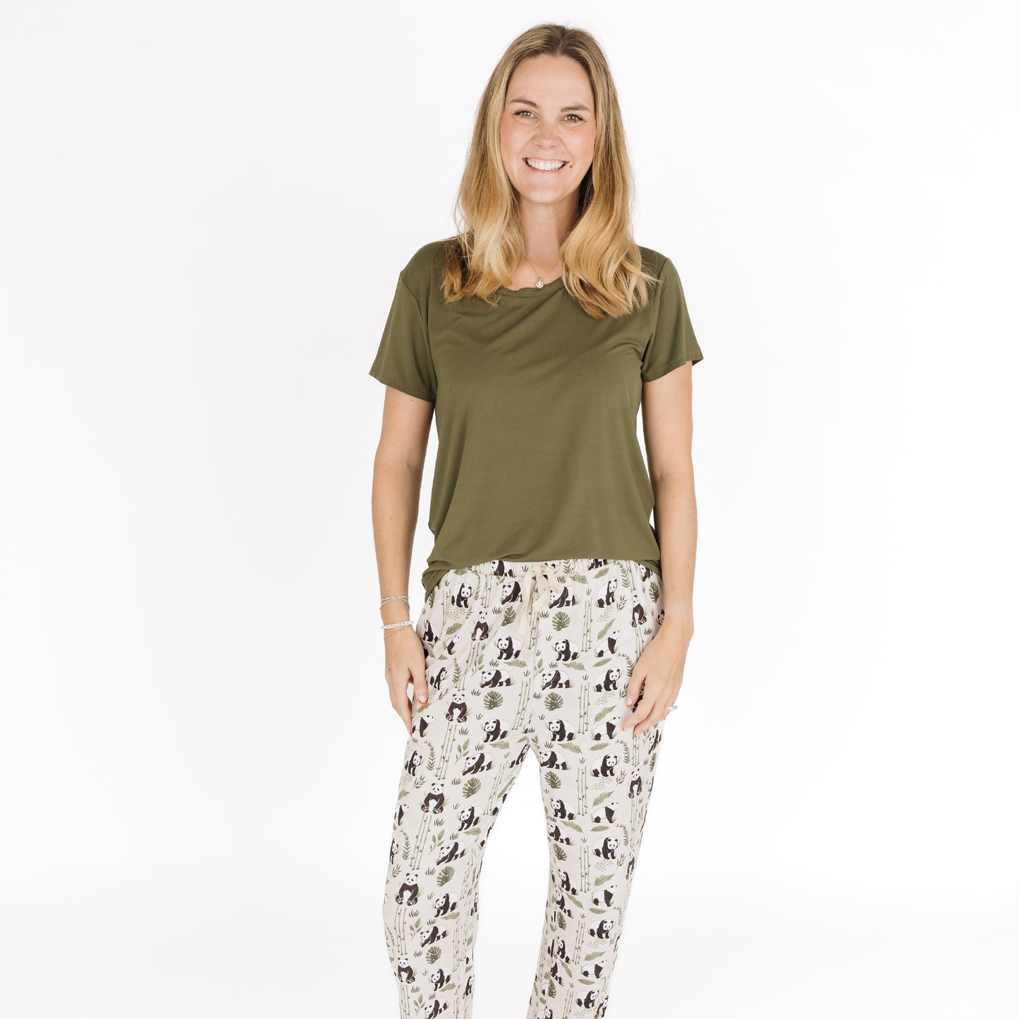 Woman wearing an olive green top and patterned pants on a white background