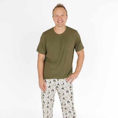 Man wearing an olive green t-shirt and patterned pants on a white background