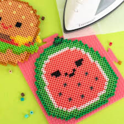 Watermelon and burger Squishmallows Perler bead designs on a green background with an iron in the corner.