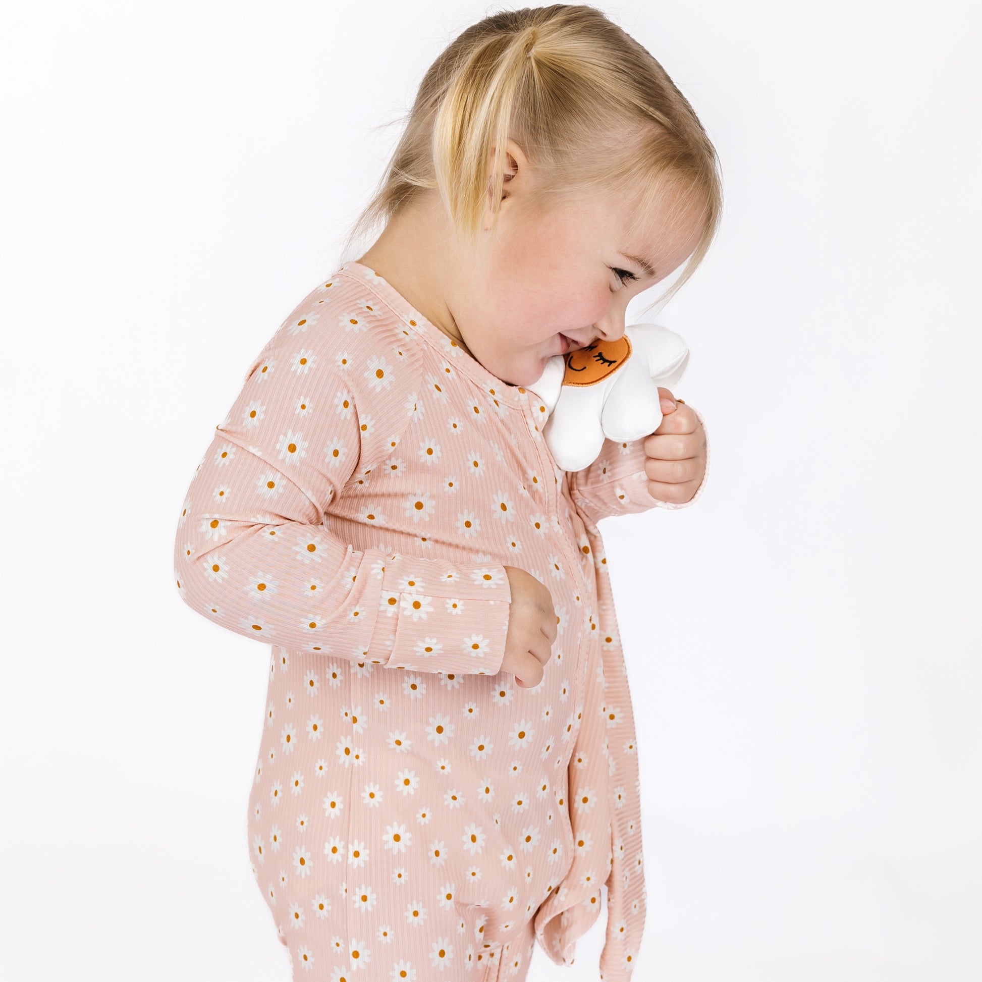 Child wearing a pink floral outfit holding a white toy with a smiley face on a white background