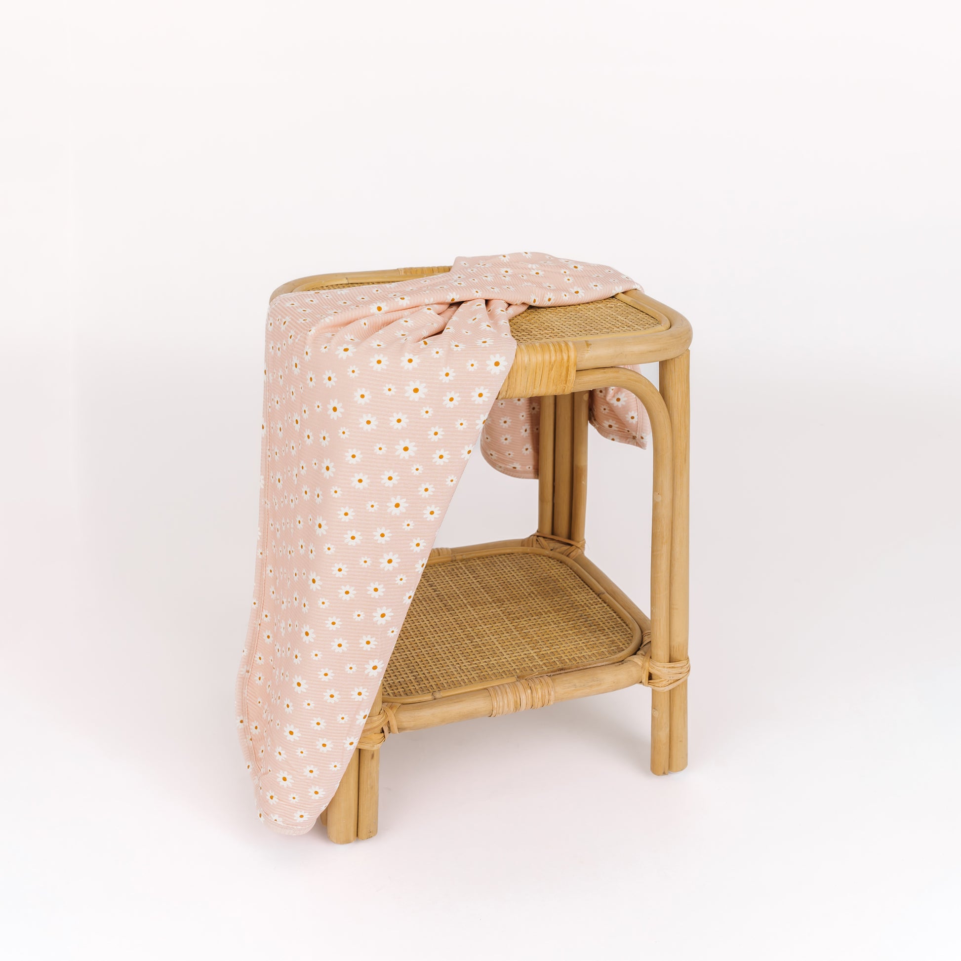 Wicker side table with a pink floral-patterned cloth draped over it on a white background