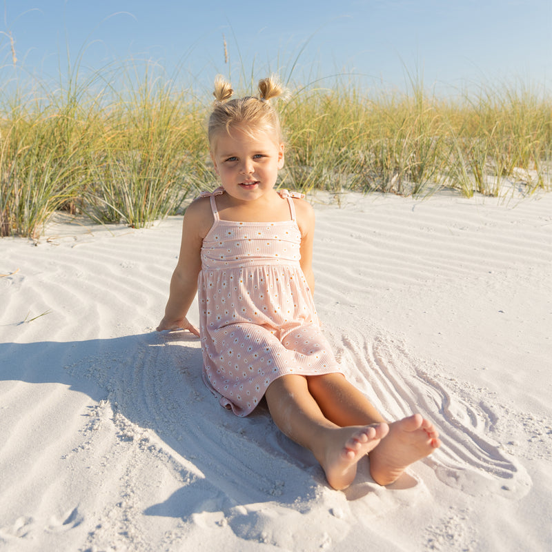 Young girl in a pink dress sitting on a sandy beach with grasses in the background