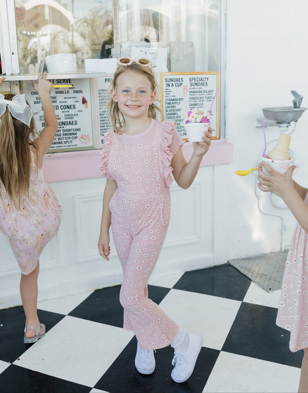 Young girl in a pink outfit standing on a black and white checkered floor with a checkered wall in the background.