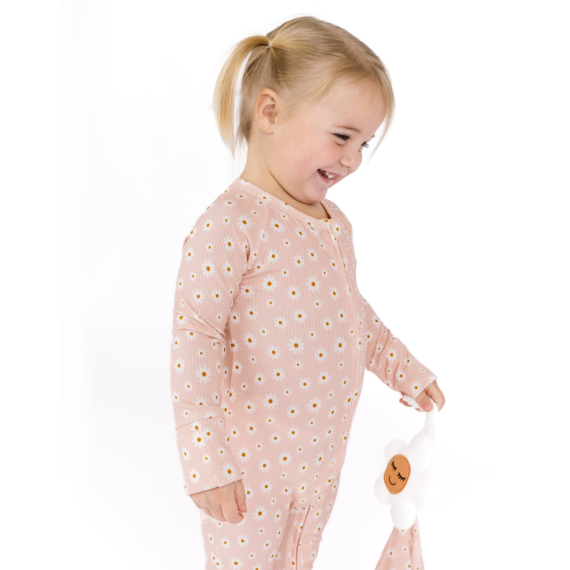 Child wearing a pink outfit with a pattern, holding a white bag with a smiley face on a white background