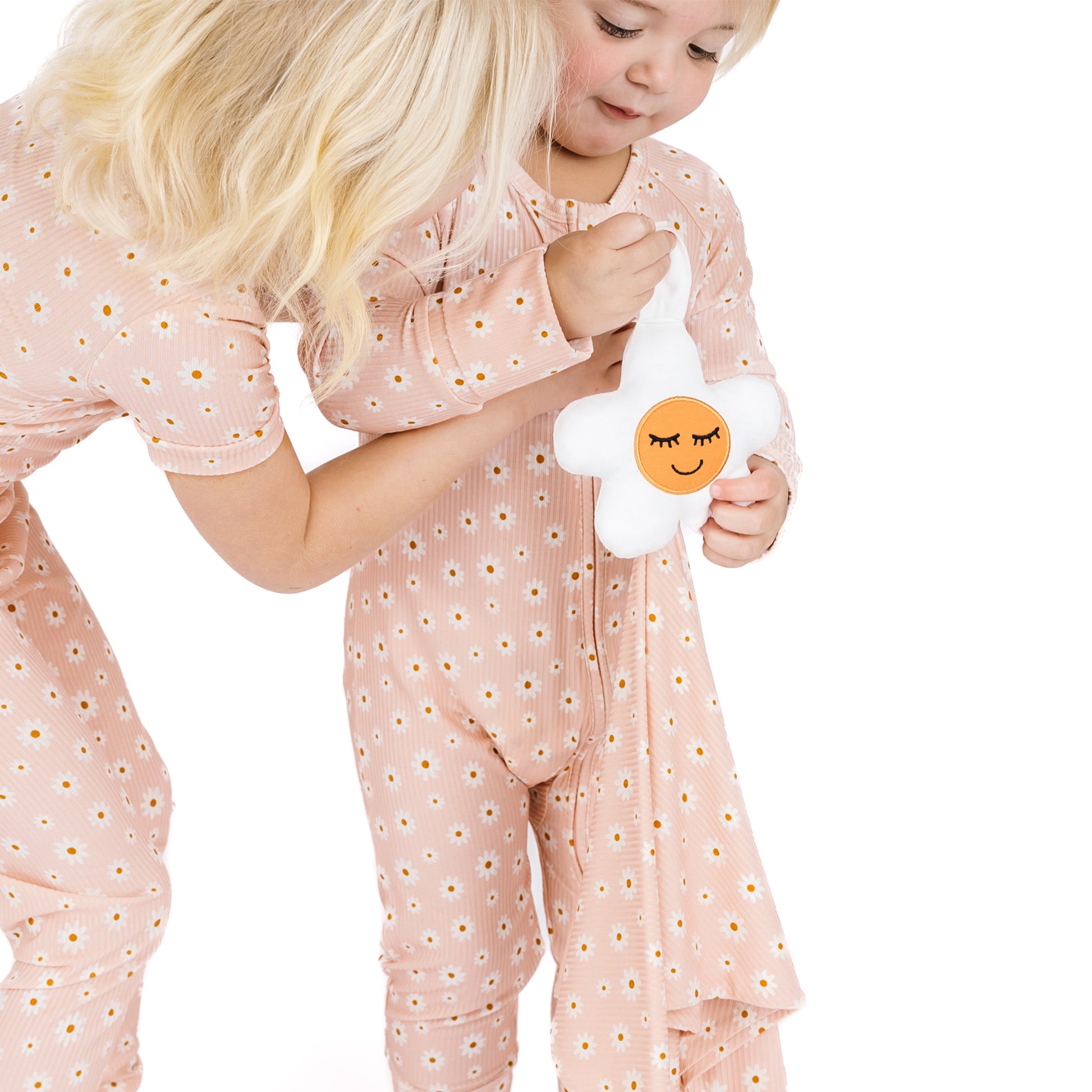 Child in pink floral pajamas holding a plush toy with a face on a white background