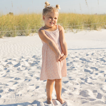 Young girl in a pink dress standing on a sandy beach with grass in the background