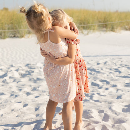Two young girls hugging on a sandy beach with a blurred natural background