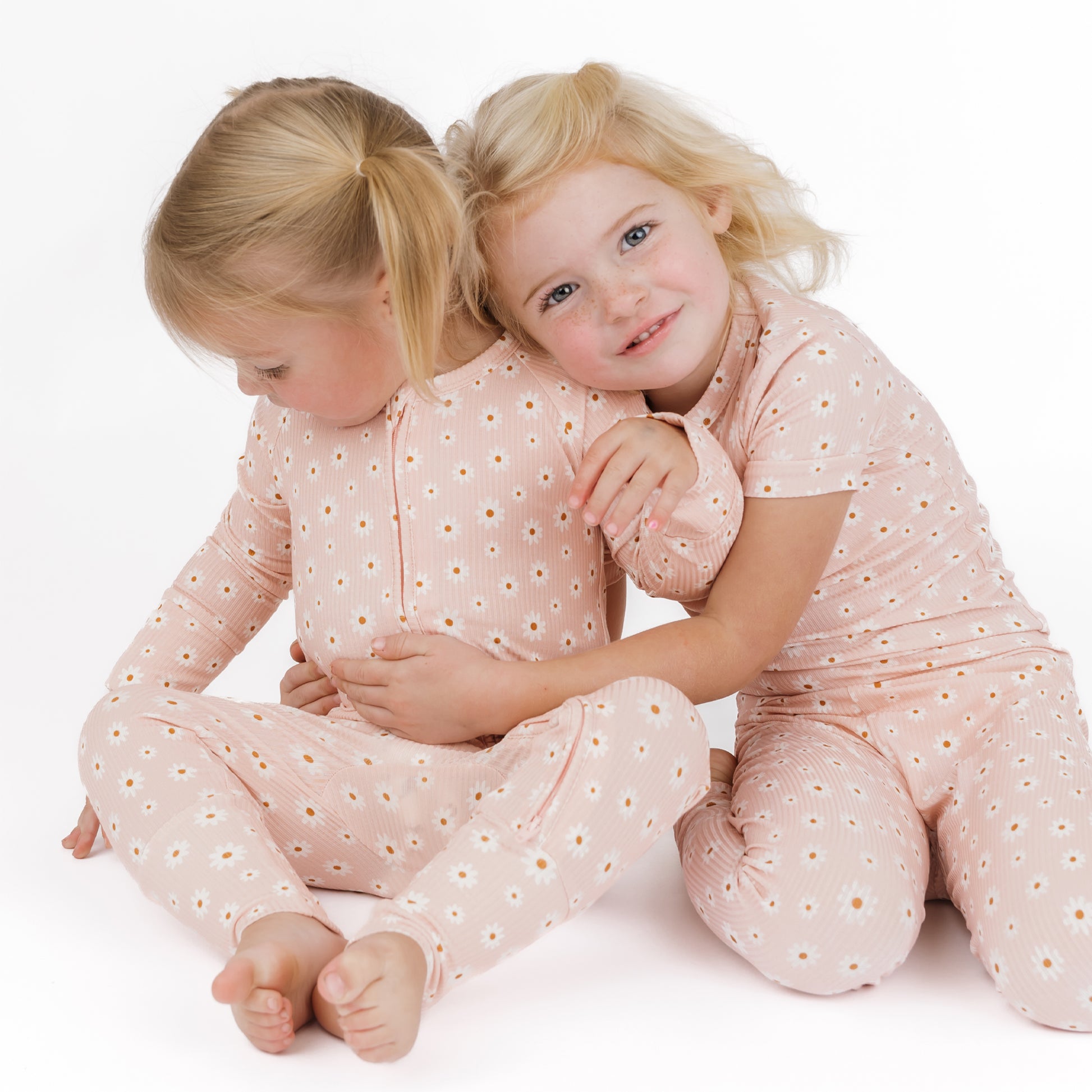 Two young girls in matching pink outfits with white polka dots sitting on a white background.