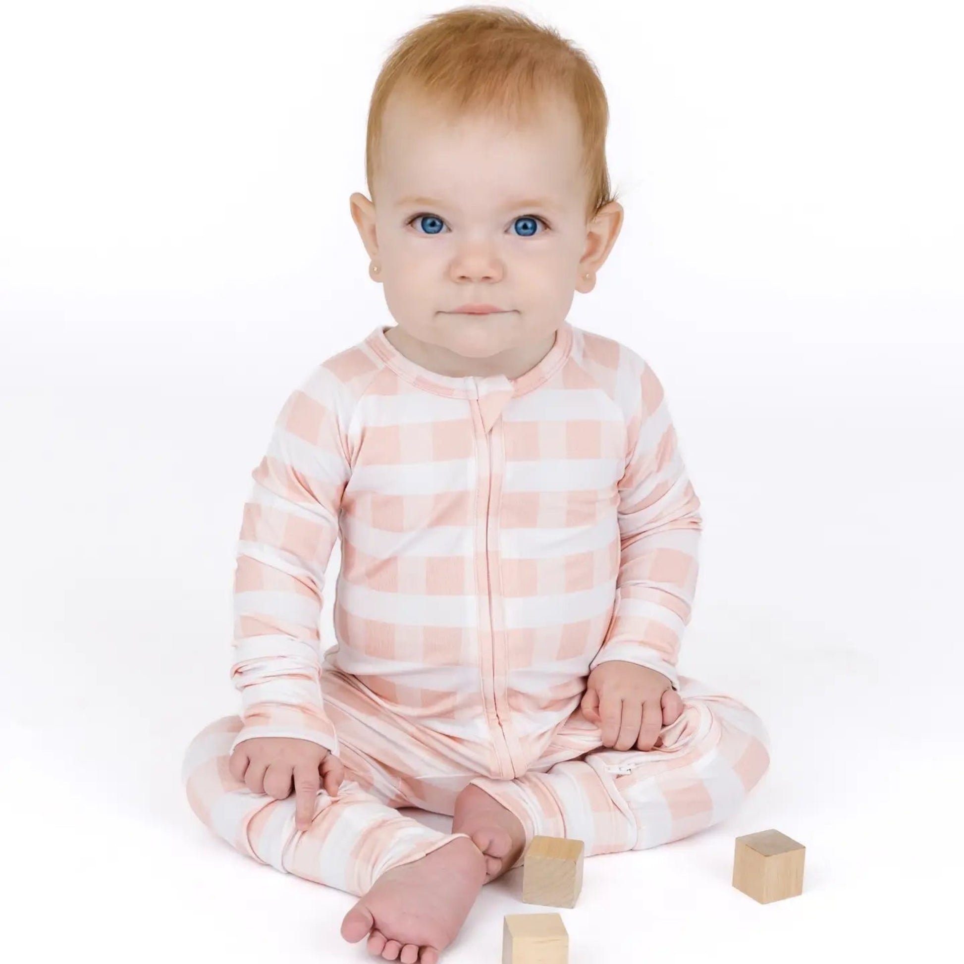 Baby in a pink and white striped onesie sitting on a white background with wooden blocks.
