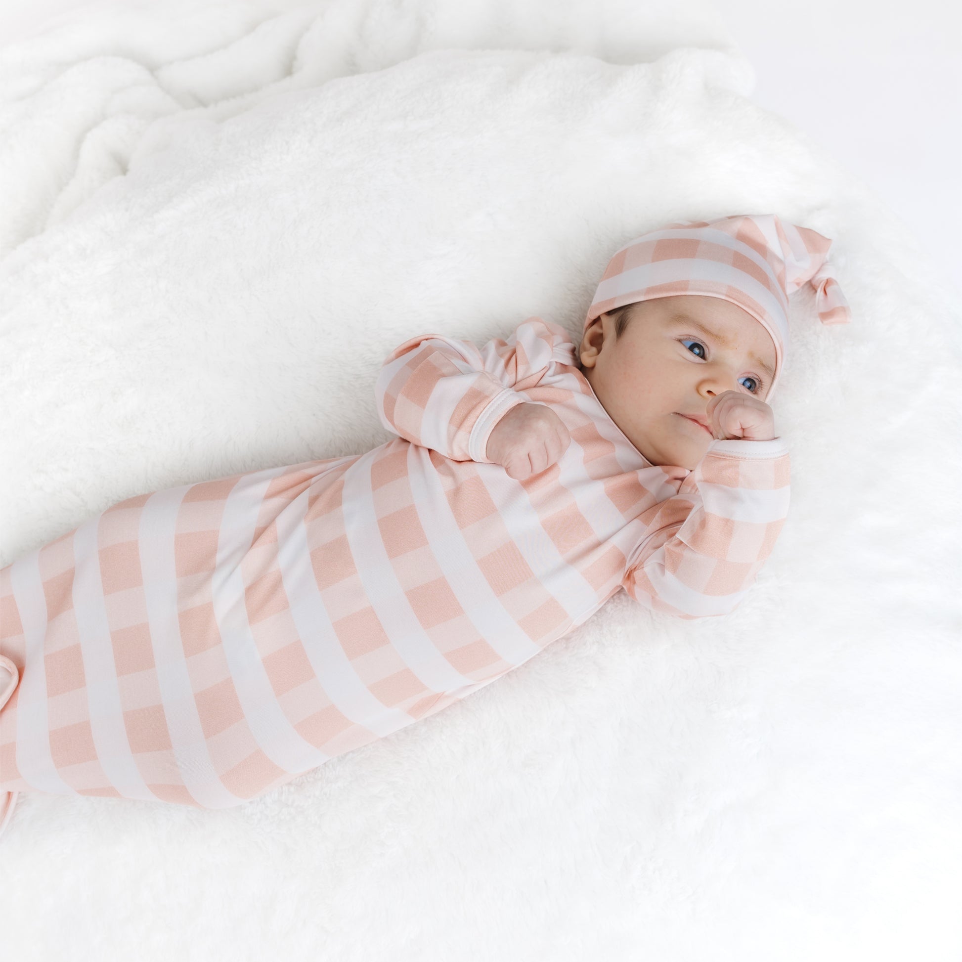 Baby swaddled in a pink and white striped blanket with matching hat on a white background