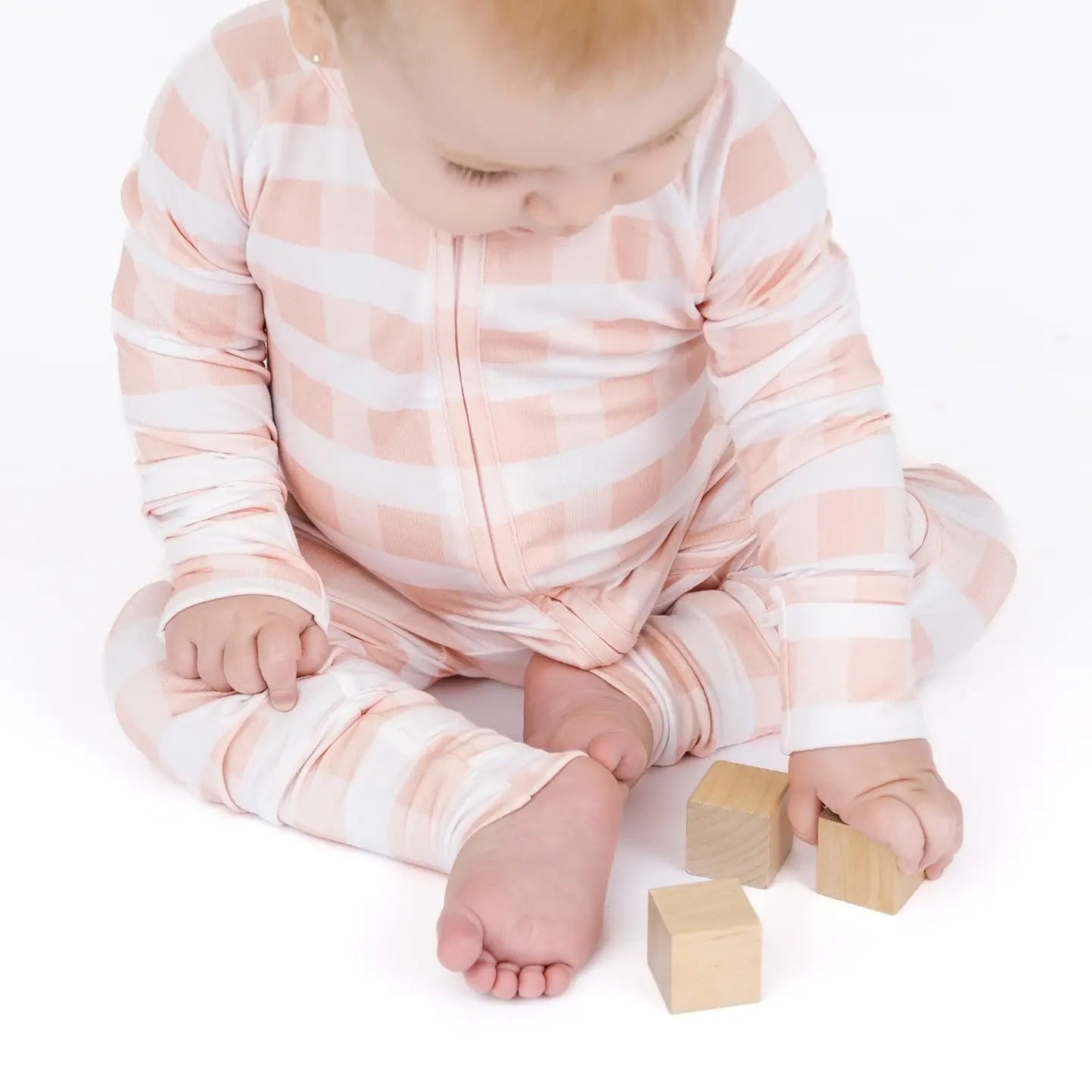 Baby in a pink and white striped onesie sitting on a white surface with wooden blocks.
