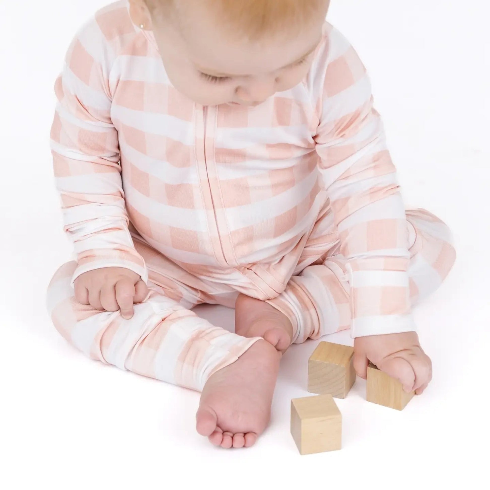 Baby in a pink and white striped onesie sitting on a white surface with wooden blocks.