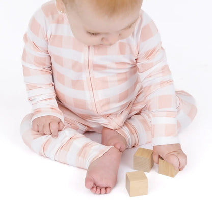 Baby in a pink and white striped onesie sitting on a white surface with wooden blocks.