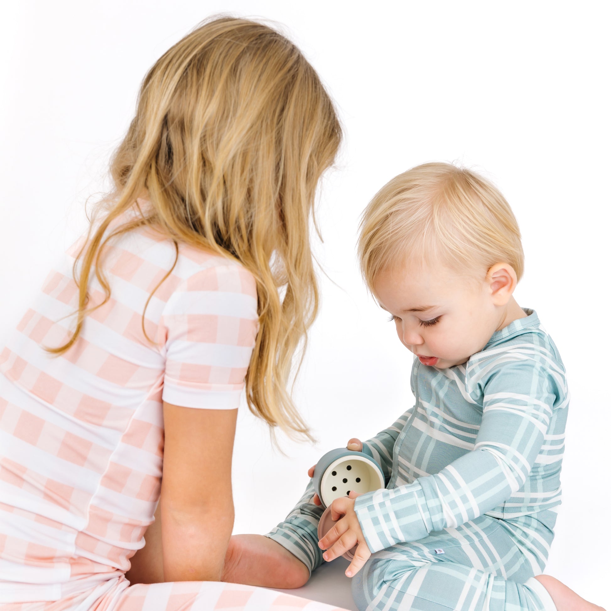 Two children sitting on a white background, one holding a small container.