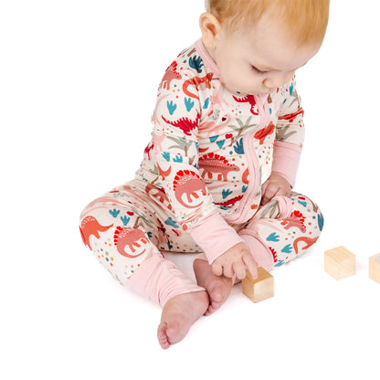 Baby sitting in bamboo zip pajama with playful dinosaur print.